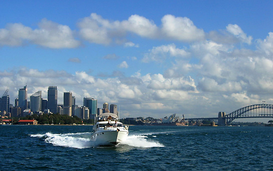 motor yacht speeding around Sydney Harbor with the city skyline and Sydney Harbour Bridge in the background