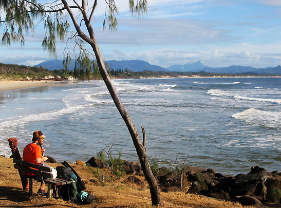 visitor strumming a guitar on a bench overlooking the beach, Byron Bay